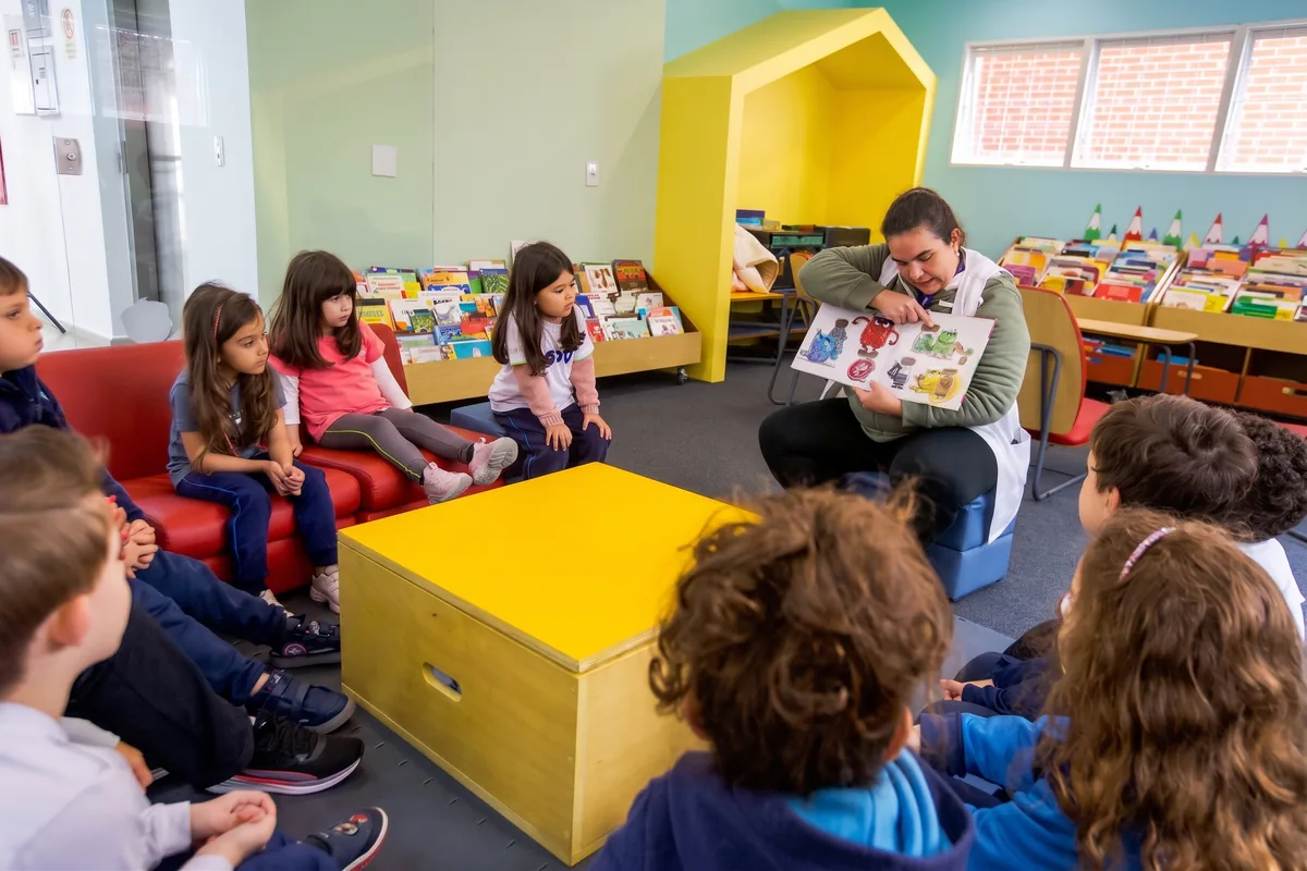 Professora do GDV lendo um livro ilustrado para crianças da Educação Infantil na biblioteca